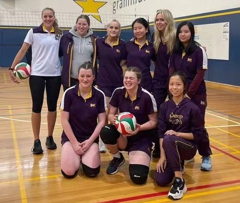 8 students and their coach from a volleyball team pose in two rows