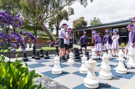 Young children in school uniform playing on a giant chessboard