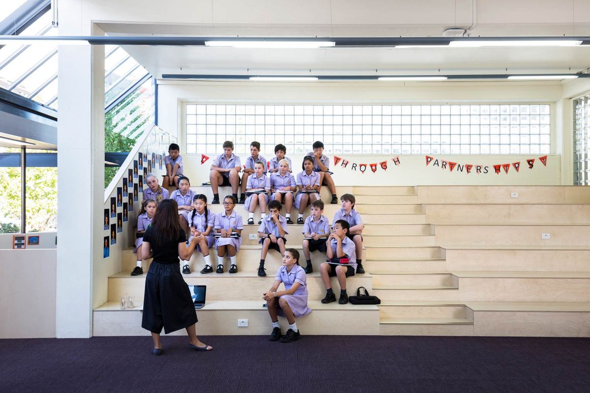 Teacher and a class of students sitting on steps inside the Wells Centre