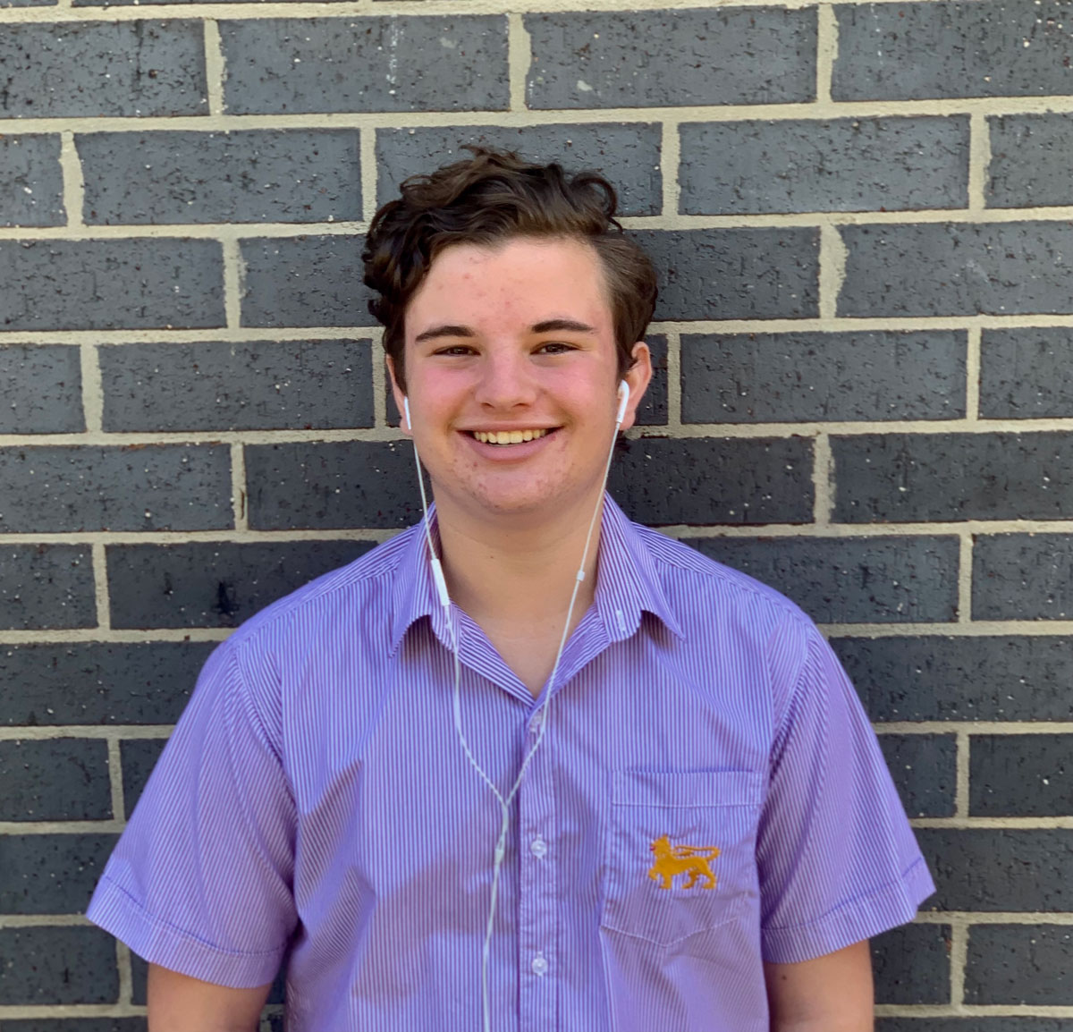 Cody Brits Cody Brits stands in front of a brick wall in his Wesley uniform shirt and with headphones in